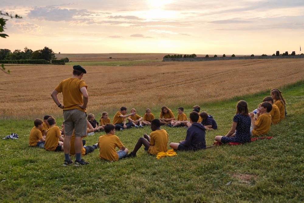 Des jeunes en t-shirts de camp, assis en cercle dans l'herbe au coucher du soleil